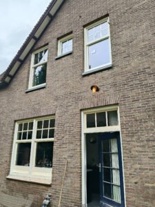 Fasada domu z cegły z nowo zamontowanymi białymi oknami i ciemnymi drzwiami wejściowymi.